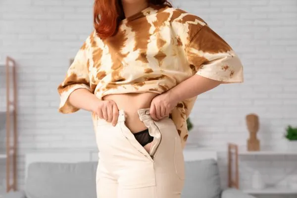 Image of woman trying to do her trousers up after pregnancy weight gain Welford on Avon